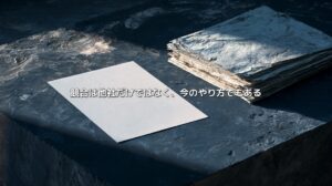 暗い石の台に置かれた白い一枚の紙と、使い込まれた紙の束。「競合は他社だけではなく、今のやり方でもある」という文字が重なる。