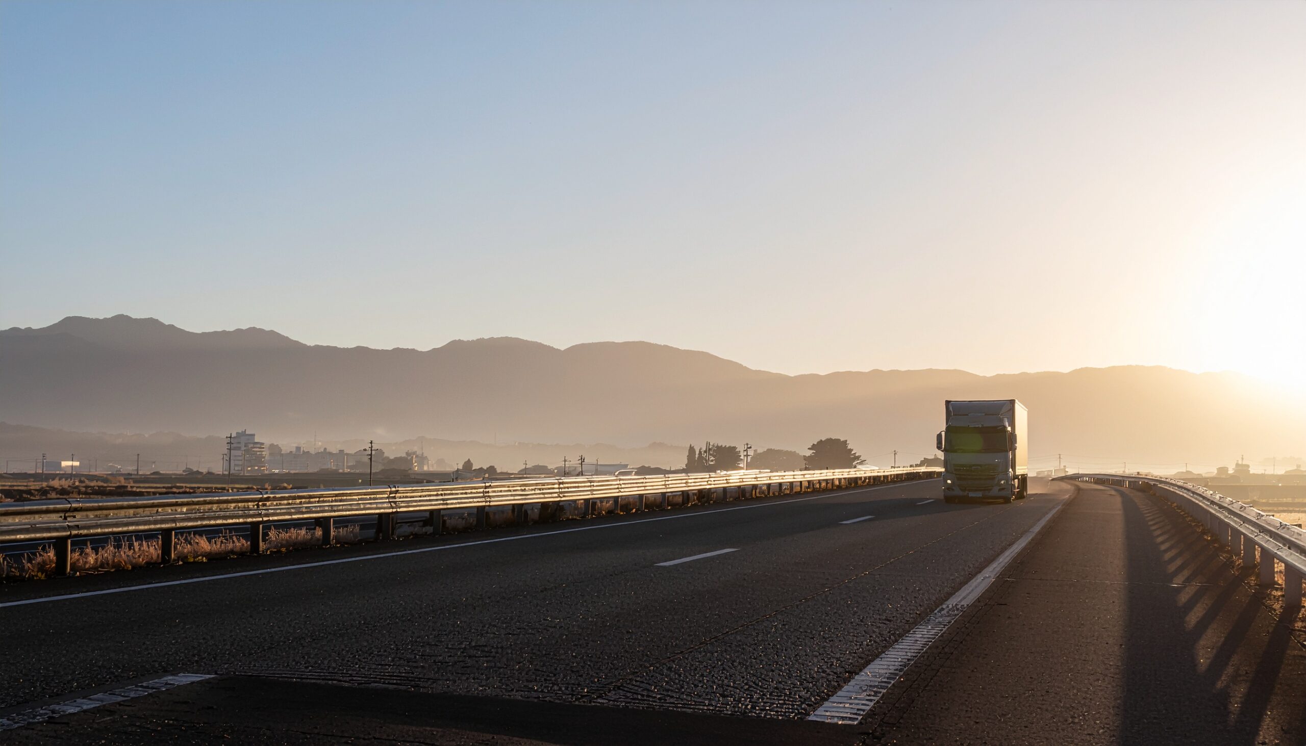 朝の光の中、高速道路を走る大型トラック。物流の未来と国際人材の共創を象徴する風景。