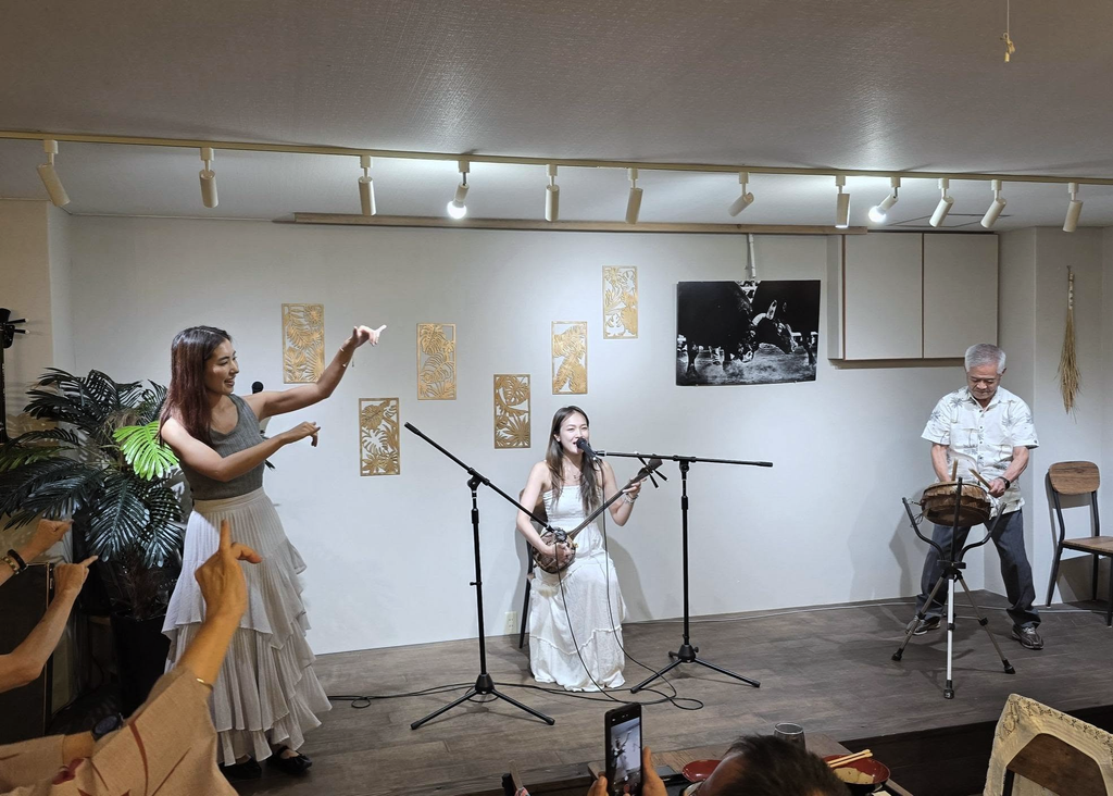 三線を弾きながら島唄を歌う成瀬茉倫さん、踊る田向美春さん、太鼓奏者に手拍子を送る参加者