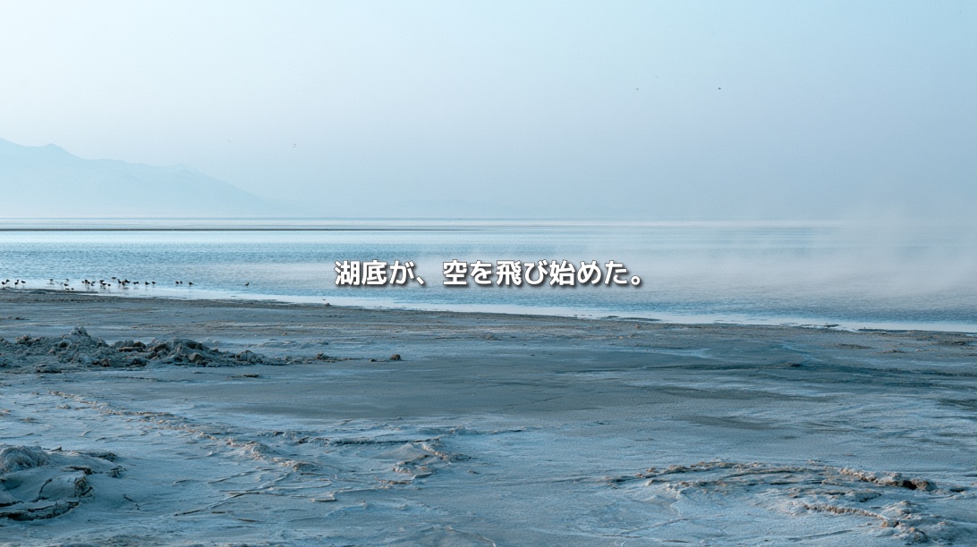 乾燥して露出したグレートソルト湖の湖底と、霧にかすむ水面に「湖底が、空を飛び始めた。」の文字を重ねたイメージ