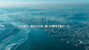 大阪湾と淀川周辺の水辺、大阪市の高密度な都市景観、湾岸の港湾エリアを俯瞰した風景。川と海と商いが大阪の都市圏を形づくってきたことを表現したアイキャッチ画像。