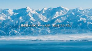 富山湾の向こうに雪をいただく立山連峰が広がる富山県の風景。「高低差4,000メートルが、富山をつくった。」の文字入り